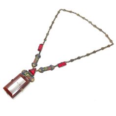 This beautiful necklace, reflects the craftsmanship and eye for detail characteristic of Czechoslovakian jewellery design.  Condition Report: Excellent The Details... This gilded metal necklace features pressed metal bow designs along its length. At the centre of the necklace, there are emerald and triangular cut, claw set, red glass panels. There are also gilded metal panels detailed with geometric designs that are accented with red, blue and green enamel. Suspended from the centre of the neckl Antique Rectangular Pendant Necklace For Formal Occasions, Vintage Red Cabochon Necklace, Red Vintage Cabochon Necklace, Red Vintage Necklace With Cabochon, Glass Pendant Necklace With Cabochon, Red Medallion Amulet Necklace, Art Deco Red Rectangular Jewelry, Red Rectangular Art Deco Jewelry, Red Medallion Necklace For Formal Occasions