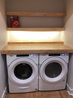 a washer and dryer in a small room with wooden shelves above the washers