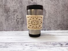 a crocheted coffee cup cozying in front of a concrete wall with a black lid