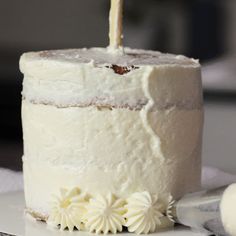 a white cake sitting on top of a plate with a candle in the shape of a flower