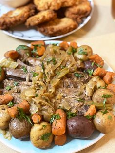 a plate with potatoes, carrots and meat on it next to some fried chicken