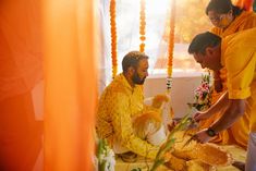 three men in yellow outfits are preparing food on a table with flowers and garlands