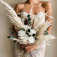 a woman in a white dress holding a bouquet of flowers and pamodia leaves