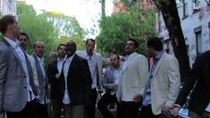 a group of men standing next to each other in front of some trees and buildings