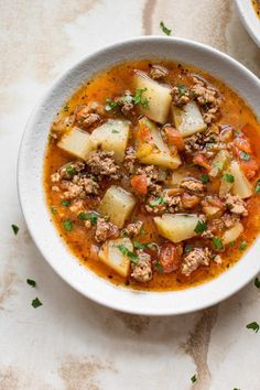 two white bowls filled with soup on top of a marble counter topped with meat and veggies