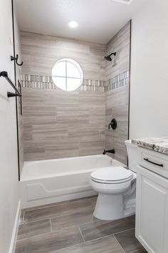 a white toilet sitting next to a bath tub in a bathroom under a round window