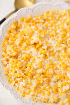 a bowl filled with corn on top of a white plate next to a gold spoon