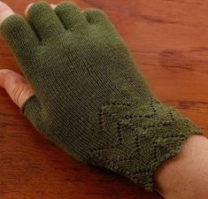 a person's hand wearing green knitted gloves on top of a wooden table