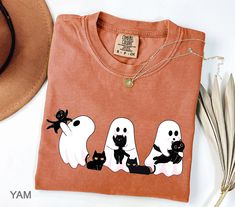 an orange t - shirt with ghost and black cats on it next to a straw hat