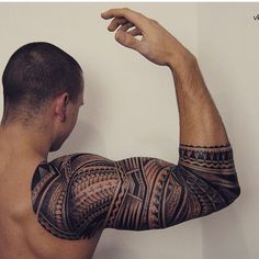 a man with a tattoo on his arm and shoulder is standing in front of a white wall