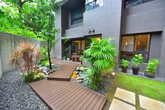 a wooden deck in front of a house surrounded by trees and plants on either side of the walkway