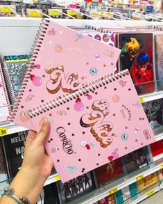 a person is holding up a pink notebook with stickers on it in a store