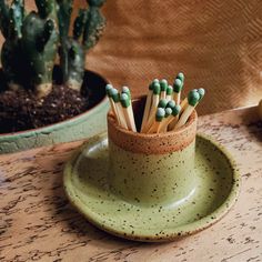 a cup filled with matchsticks sitting on top of a green saucer next to a potted plant