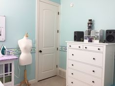 a bedroom with blue walls and white furniture in the foreground is a mannequin's head