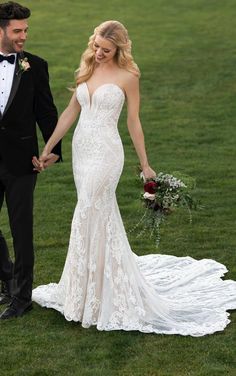 a bride and groom hold hands as they walk through the grass in their wedding gown