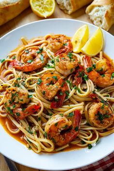 a plate of pasta with shrimp and lemons on the side, next to bread