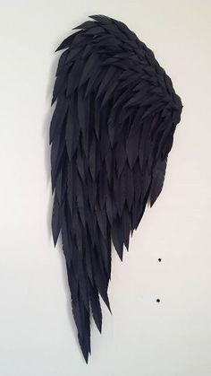 an artistic piece of art made out of black feathers on a white wall with one wing missing