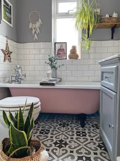 a pink bath tub sitting next to a white toilet in a bathroom under a window