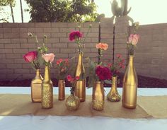 six gold vases with flowers in them sitting on a table next to a brick wall