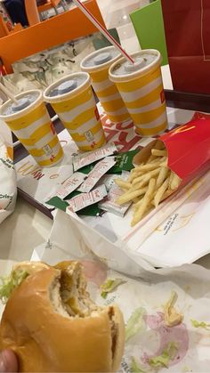 a person holding a sandwich and french fries in front of two cups of sodas