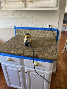 a kitchen counter being painted white with blue tape on the edge and a drill in the middle