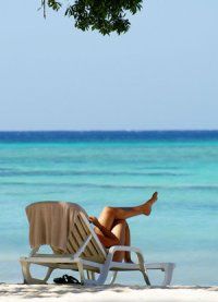 a woman laying on top of a white beach chair under a tree next to the ocean