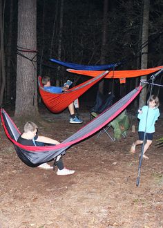 two children playing in hammocks at night with adults watching from the woods behind them