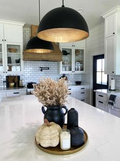 a kitchen with white cabinets and black pendant lights over the counter top, along with two vases filled with dried flowers