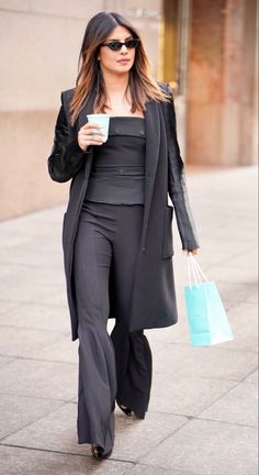 a woman is walking down the street with her coffee in hand and carrying shopping bags