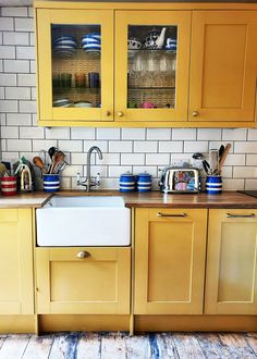 a kitchen with yellow cabinets and white tile backsplash, wooden flooring and wood floors