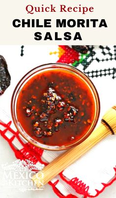 a bowl filled with sauce sitting on top of a red table cloth next to a wooden spoon