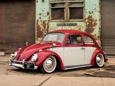 an old red and white vw bug parked in front of a rusted building