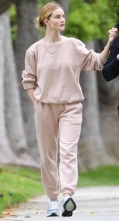 a woman is walking down the street holding hands with another woman who is wearing a sweater and pants