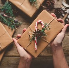 two hands holding a wrapped present with a candy cane and pine cone on the top