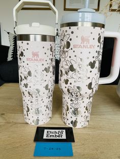 two mickey mouse travel mugs sitting on top of a table next to each other