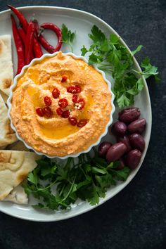 a plate with hummus, pita bread and olives on it next to red peppers