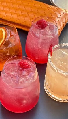 three glasses filled with different types of drinks on top of a blue table next to oranges and strawberries