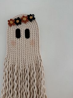 a white wall hanging with black eyes and long braids on it's sides