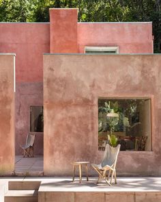 two chairs and a table sitting in front of a building with pink paint on it