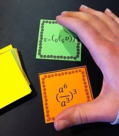 a hand is pointing at three different colored cards on a table with numbers and symbols