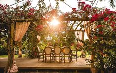 an outdoor dining area with chairs and flowers on the arbor, surrounded by greenery