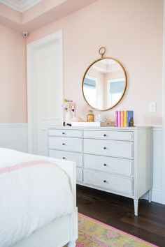 a white dresser sitting next to a bed in a room with pink walls and wooden floors