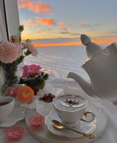 a table topped with cups and saucers filled with liquid next to a vase full of flowers