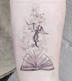 an open book with a dragon flying out of it on the side of a woman's leg