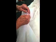 an older woman is sewing on her white dress