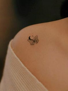 a small butterfly tattoo on the back of a woman's left shoulder, which is black and white