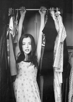 black and white photograph of a woman in front of clothes hanging on racks with her hands behind her head