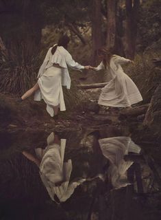 two women in white dresses are dancing by the water