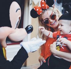 a woman holding a child in front of mickey mouse