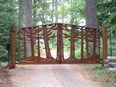 an iron gate in the middle of a dirt road with trees on each side and rocks around it